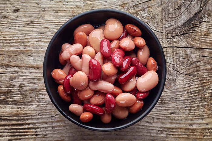 Various types of canned beans in black bowl on wooden table, top view