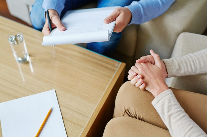 male therapist with note pad talking to woman with hands clasped