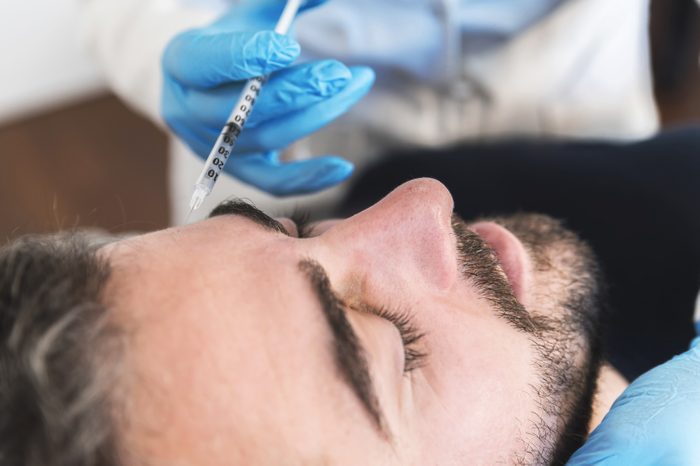 Close up of man at clinic receiving injection fillers on forehead. botox needle