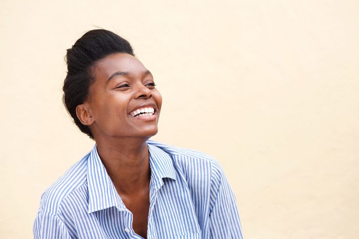 Close up portrait of beautiful young black woman laughing against wall