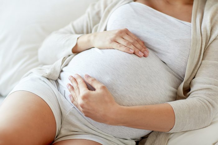 close up of pregnant woman lying in bed and touching her belly at home