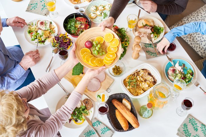 Big happy family at dinner table enjoying delicious homemade food and passing a fruit plate. 