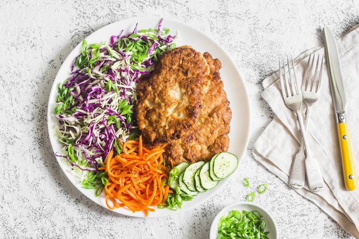 Plate of chicken schnitzel tempura, red and white cabbage coleslaw and spicy pickled carrots.