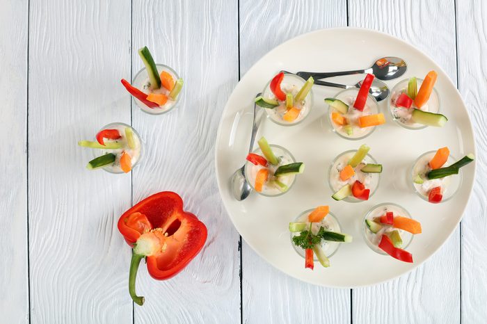 Individual cocktail shots with yogurt sauce and colorful sticks of vegetables on platter.