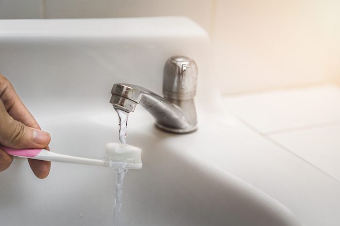 Toothbrush with toothpaste underneath running faucet