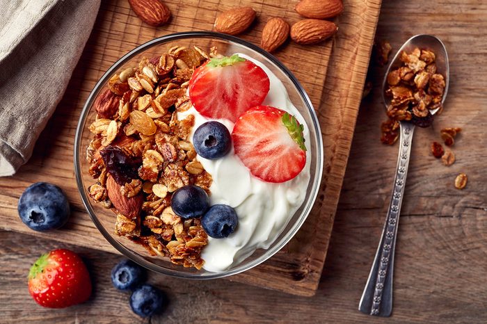 Bowl of homemade granola with yogurt and fresh berries on wooden background from top view