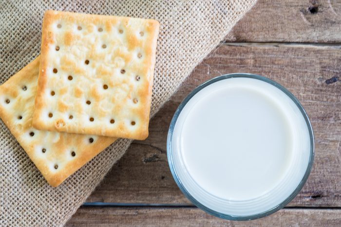 stack of crackers on gunny sack cloth on wooden table with a cup of milk, top view