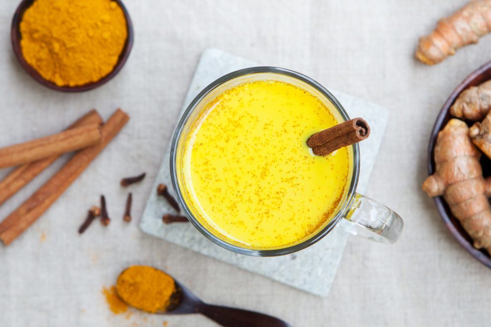 Turmeric drink, latte, tea, milk with cinnamon in a glass mug with fresh and dried turmeric on a textile grey background. Top view. Copy space.