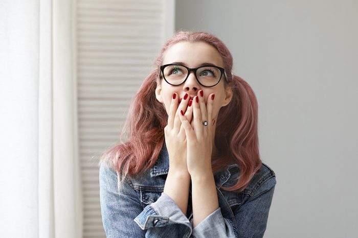 Isolated shot of fashionable young European woman with pink colored ponytails and red nails covering mouth with both hands and looking up with excited expression, overjoyed with great positive news