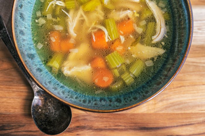 Homemade chicken soup in a turquoise bowl with an antique soup spoon on a wooden table. 