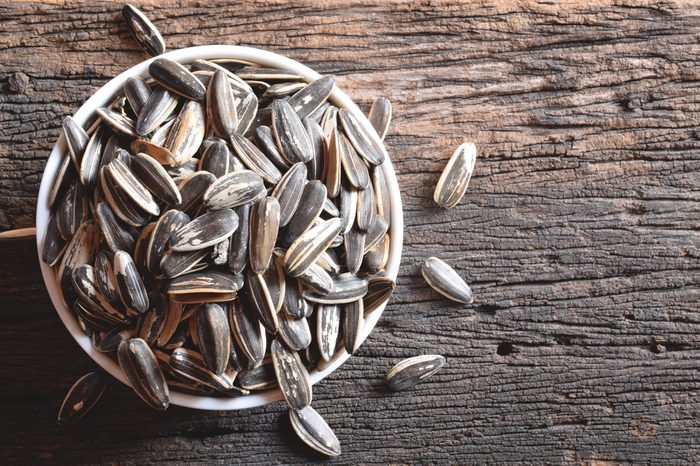 Top view of roasted sunflower seeds in white ceramic bowl on rough old wood