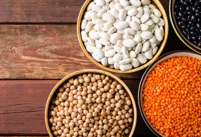 Assorted beans in bowls with red lentil, chick-pea and kidney bean on wooden background. Horizontal top view, copy space