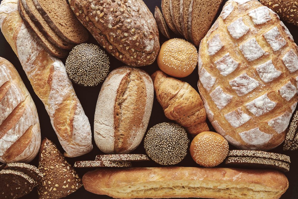 Bread background, top view of white, black and rye loaves on black