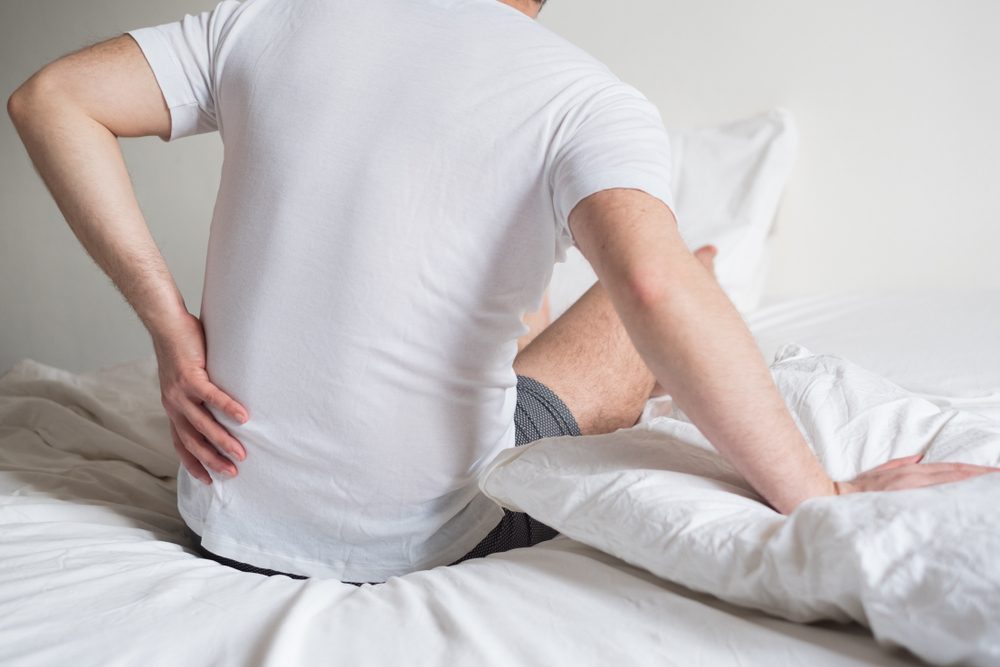 Rear view of one man sitting on bed having back pain