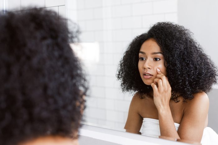 Young woman looking at mirror and examining her skin