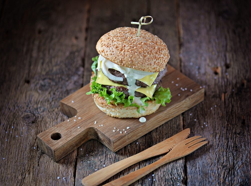 Homemade double cheeseburger with marinated onion and white sauce on a serving board