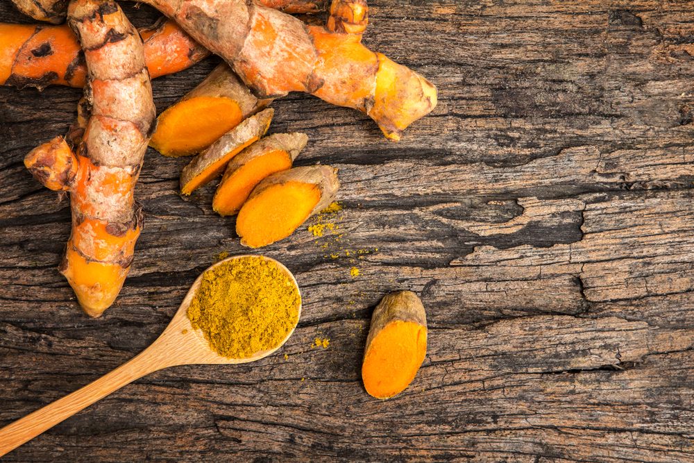 turmeric powder in spoon and roots on wooden plate