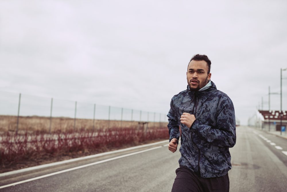 Young African man in sportswear out for a solitary run along a country road on an overcast day