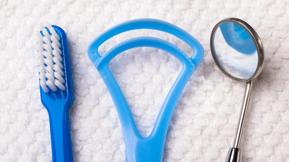 Oral hygiene health concept. Closeup dental tools blue toothbrush mirror and tongue cleaner on white towel