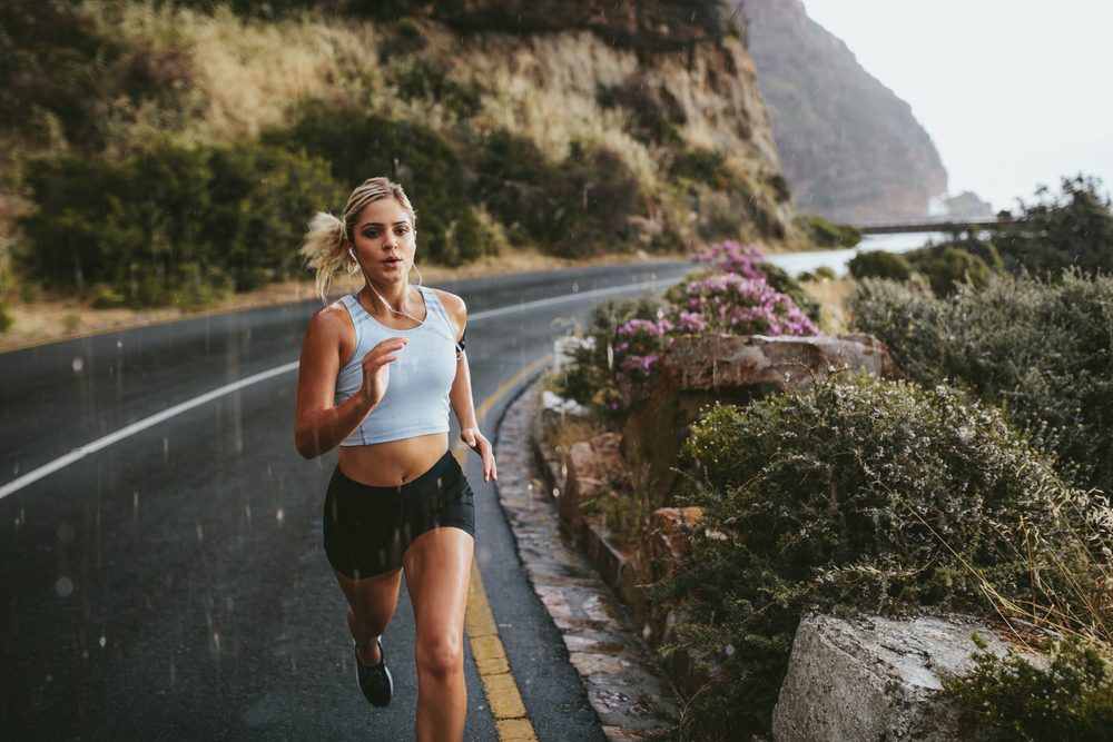 Fitness woman running on highway around the mountains. Female athlete training outdoors during rain.