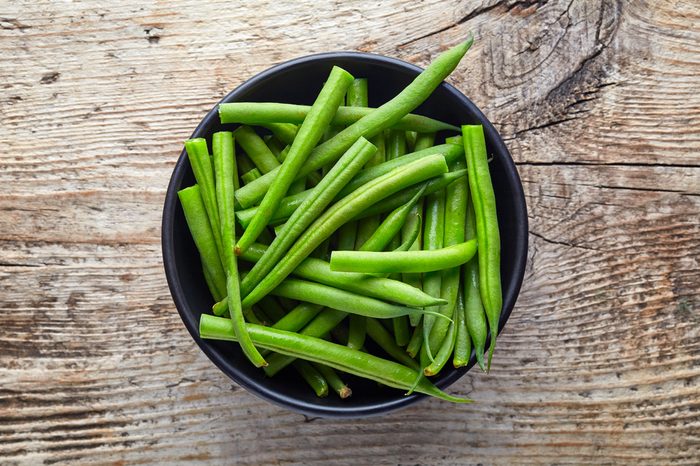 Bowl of green beans on wooden background, top view