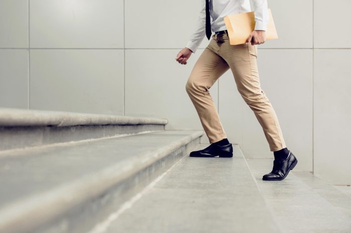 Businessman walking upstairs holding document, close up legs