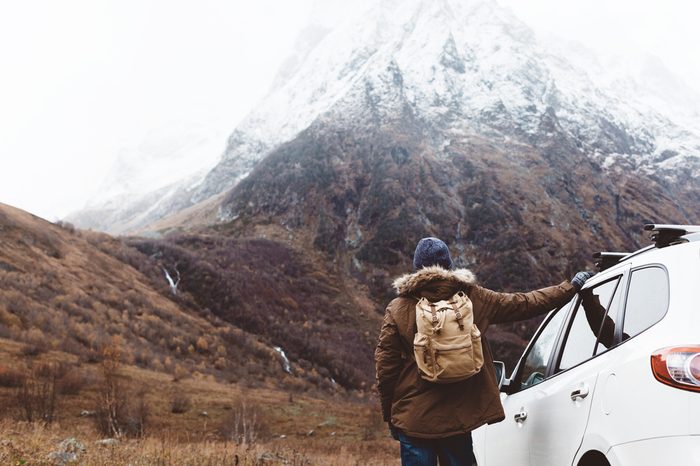 Man driving car on to the mountains. Traveler with backpack. Hiking in cold weather.