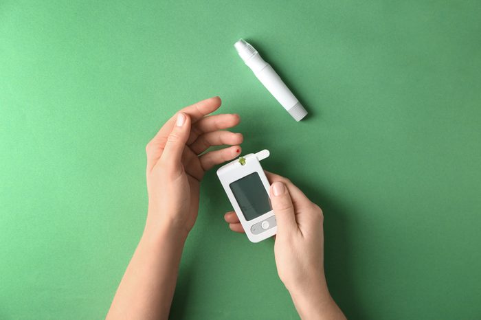 Woman measuring glucose level with digital glucometer on color background. Diabetes control