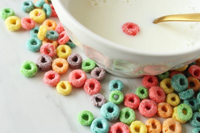 Close up view of cereal bowl with one piece of cereal and dry cereal spilled around it. Empty calories concept. Copy space.