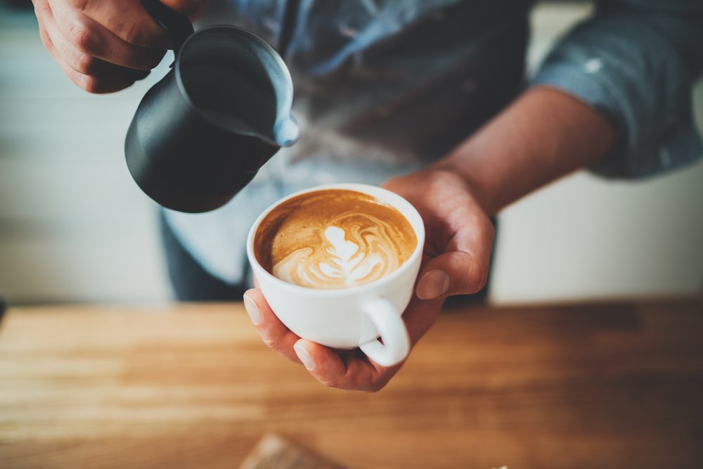 Closeup image of male barista holding and pouring milk for prepare cup of coffee, latte art, vintage color tone, coffee preparation and service concept, lifestyle