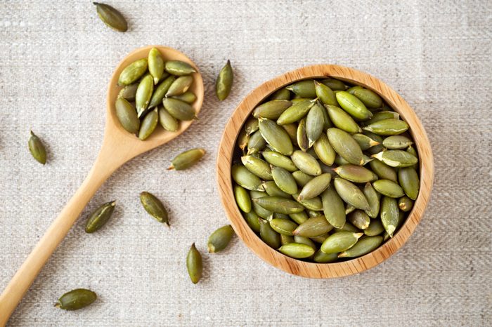 Pumpkin seeds in wooden bowl and spoon, top view