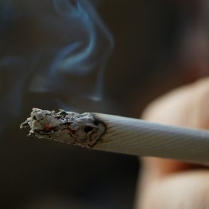 Smoking cigarette in hand with slightly defocused dark background.