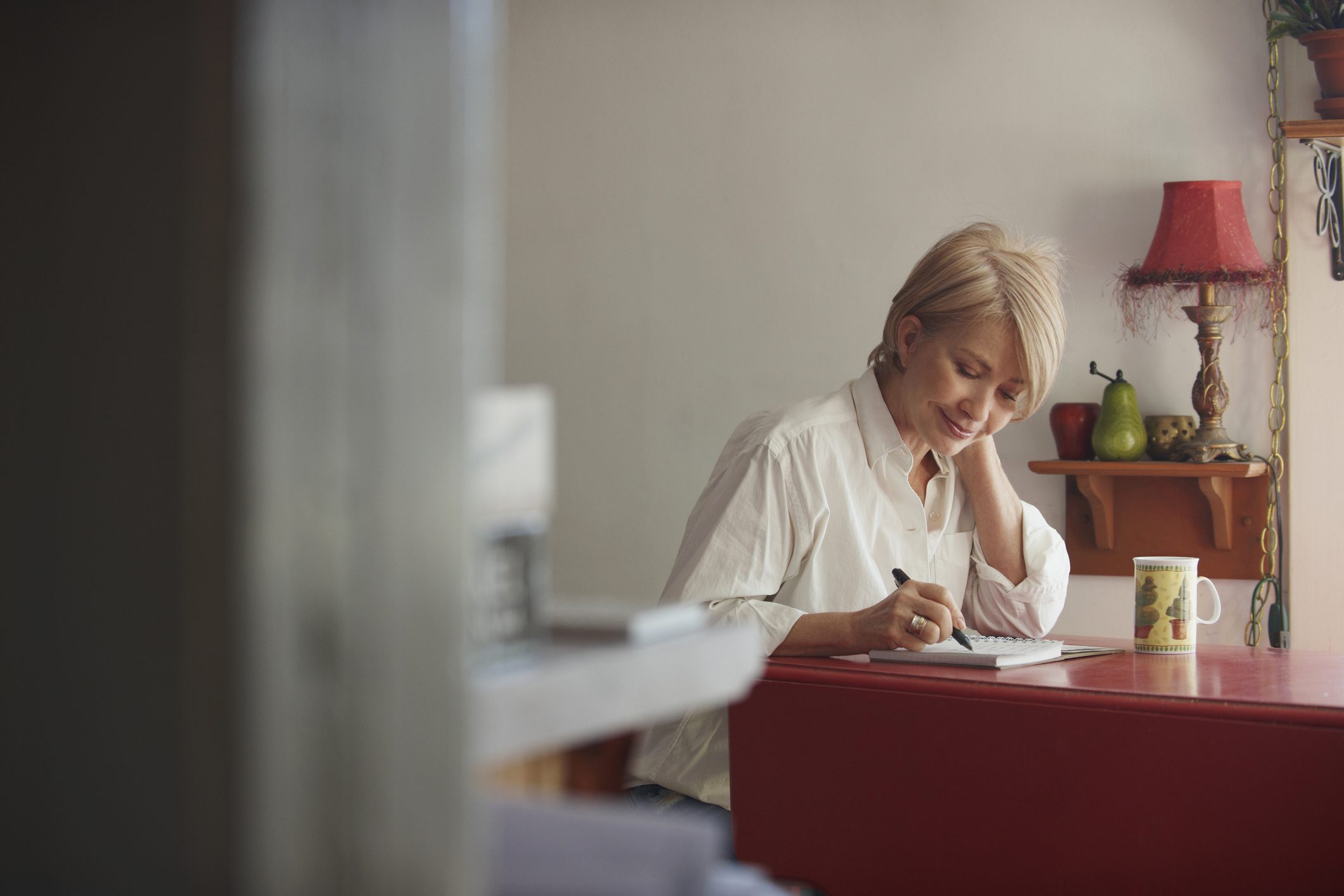 older woman writing in journal at desk