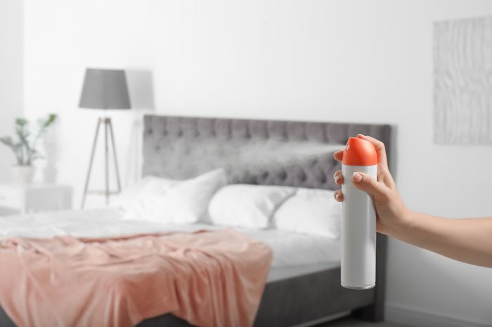 Woman spraying air freshener in bedroom