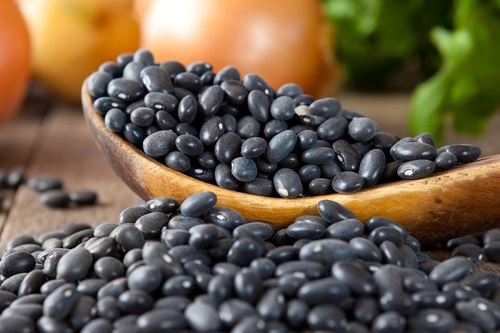 Black beans in a wooden spoon with cilantro and onions in the background