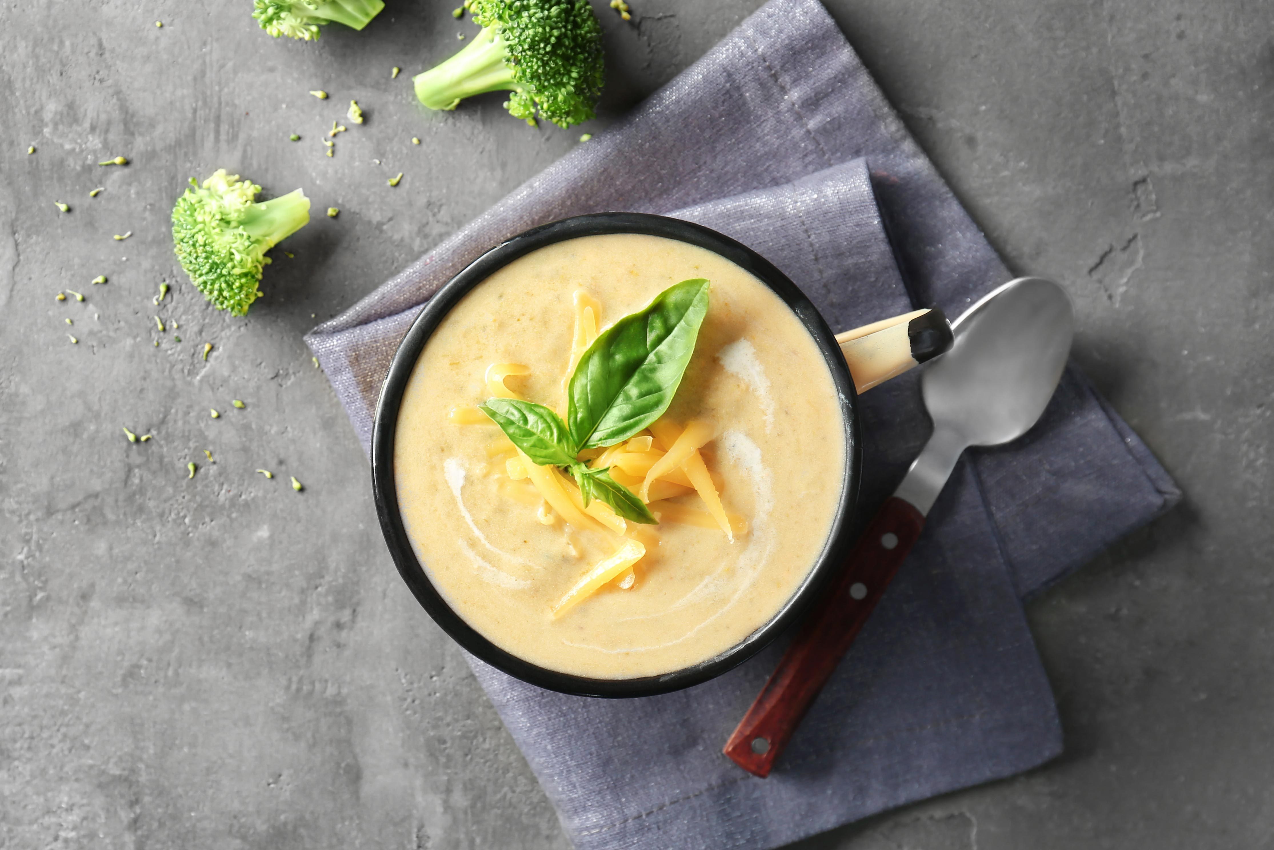 Cup with broccoli cheddar soup on kitchen table with broccoli florets