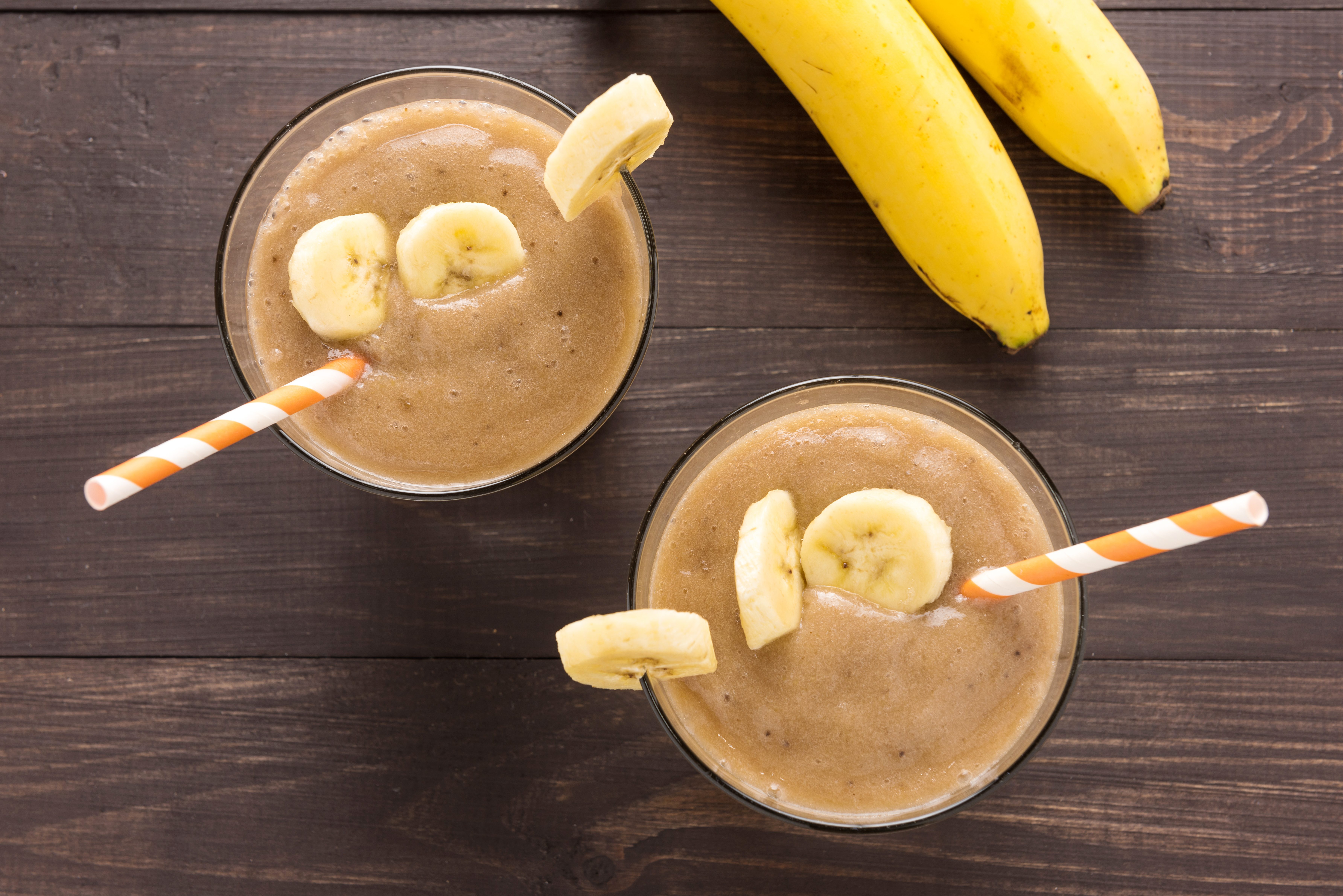 Banana smoothie and fresh banana on wooden background.