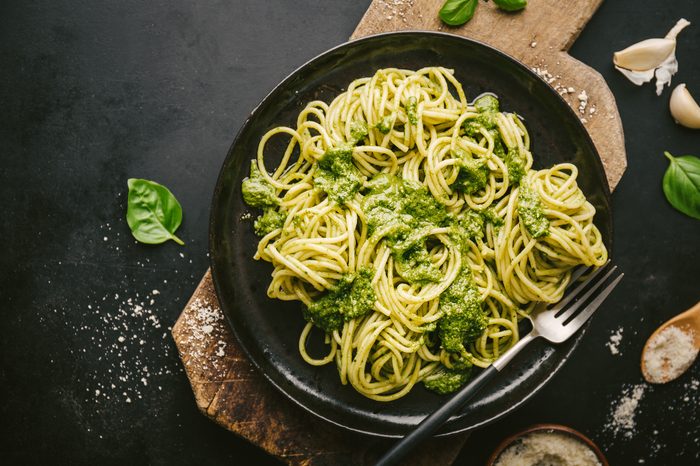 Tasty appetizing pasta spaghetti with fresh sauce pesto and cheese served on plate on black table. View from above. Ready to eat. Horizontal