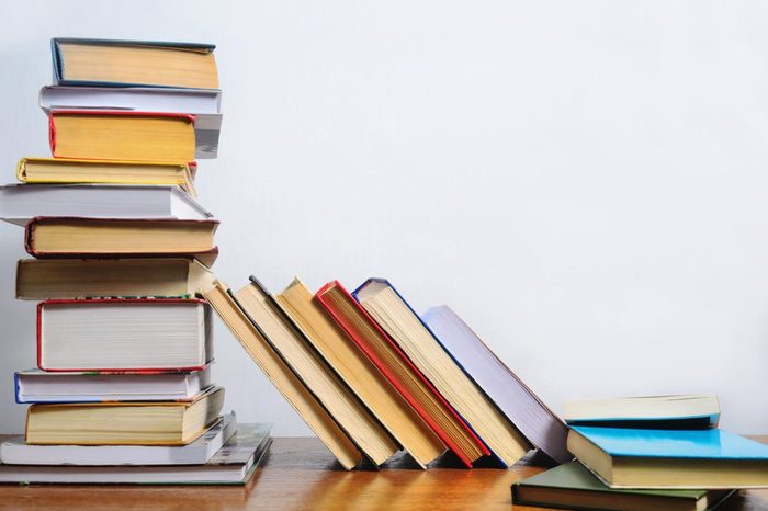 Stack of different books on a table against a white wall background