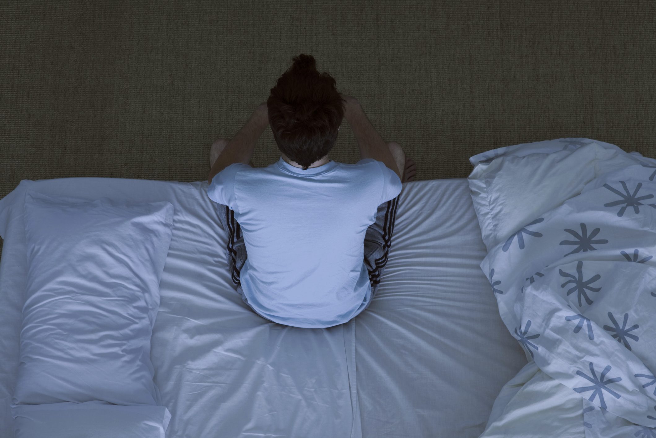 man sitting on edge of bed at night unable to sleep