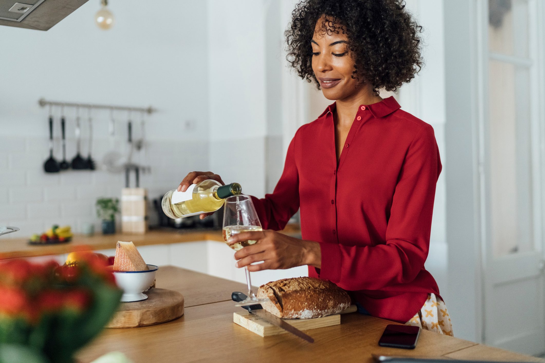 Woman standing in kitchen, pouring herself a glass of white wine