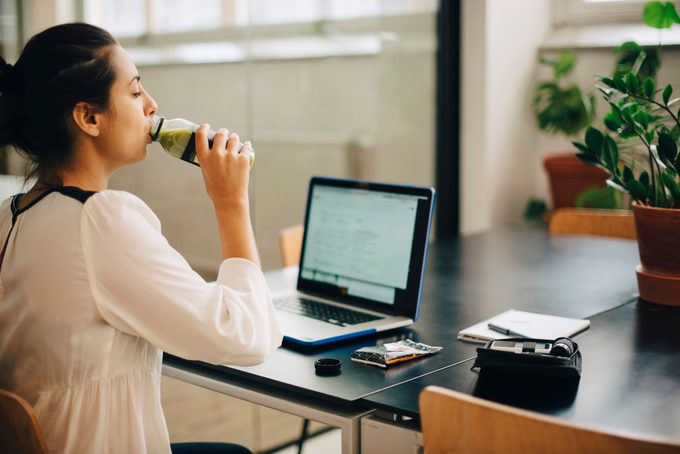 Businesswoman drinking juice while using laptop at desk in office