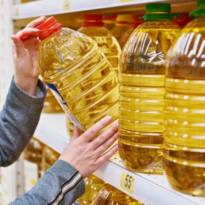 woman taking large bottle of oil off of shelf at grocery store