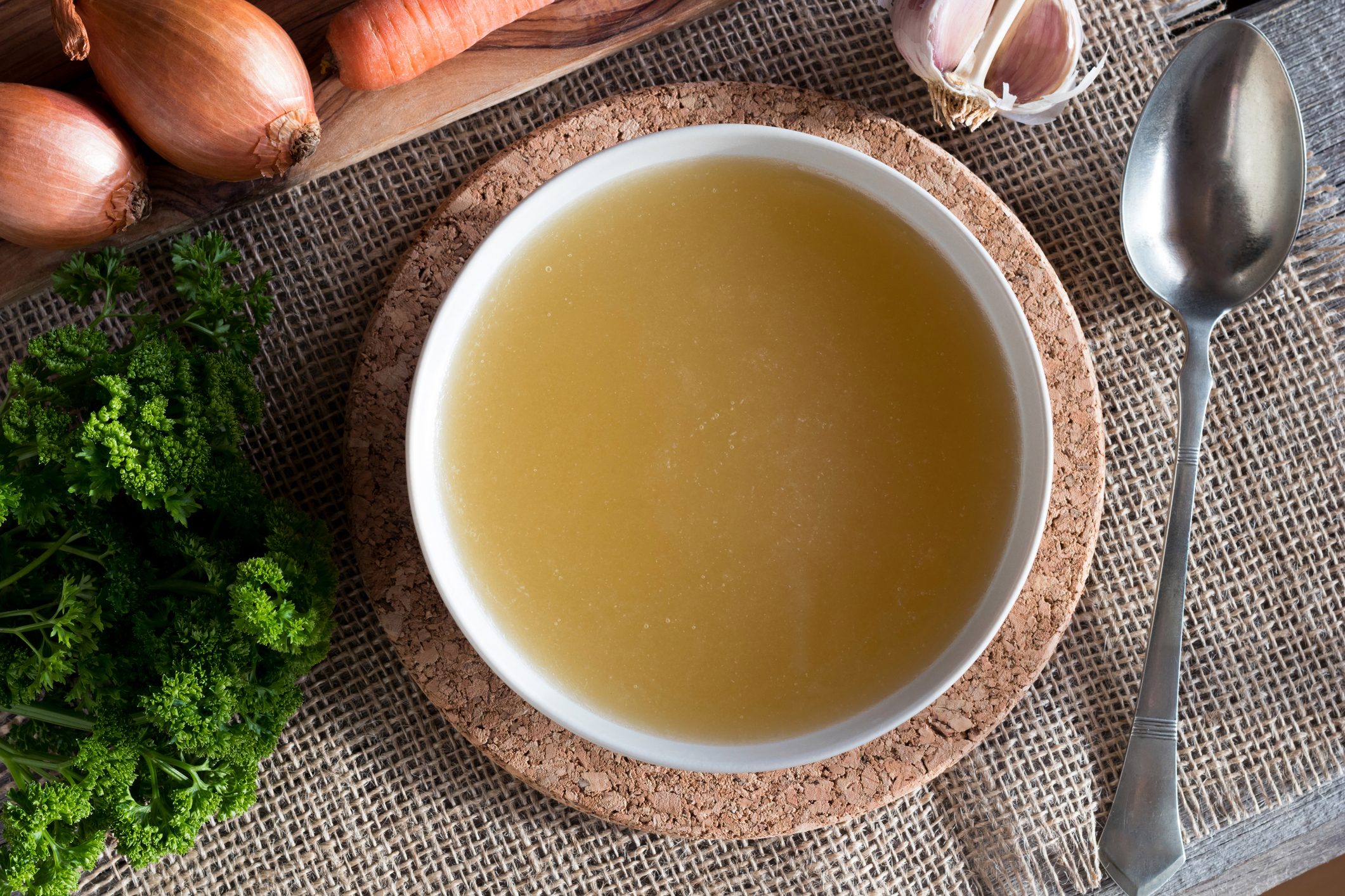 Chicken bone broth with vegetables in the background, top view