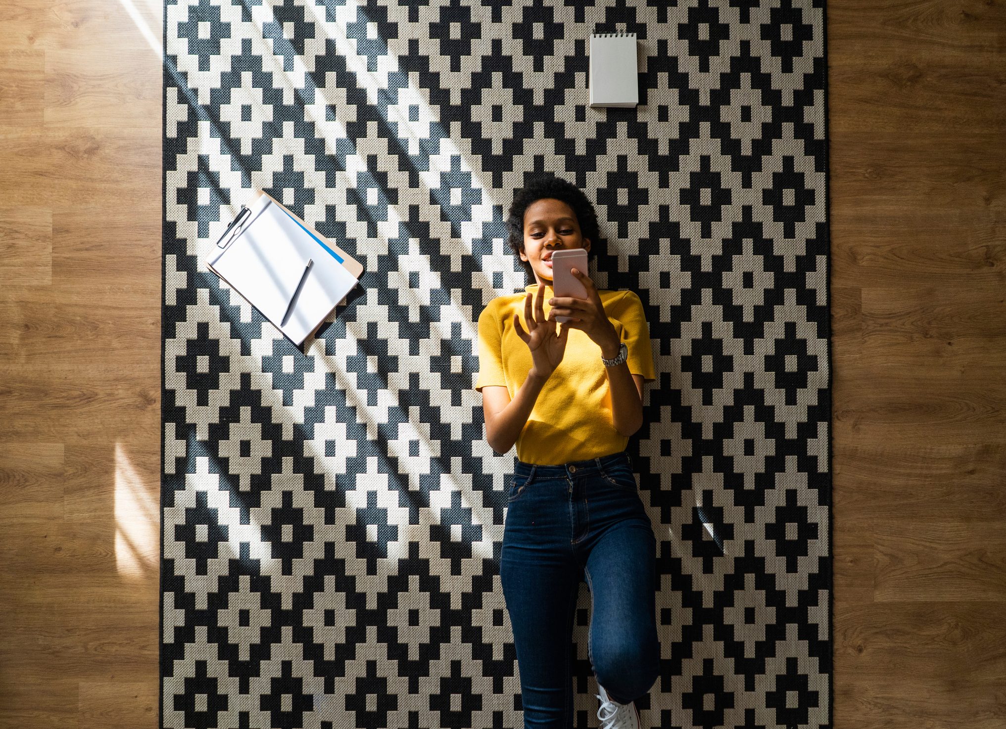 Young woman lying on carpet at home using smartphone