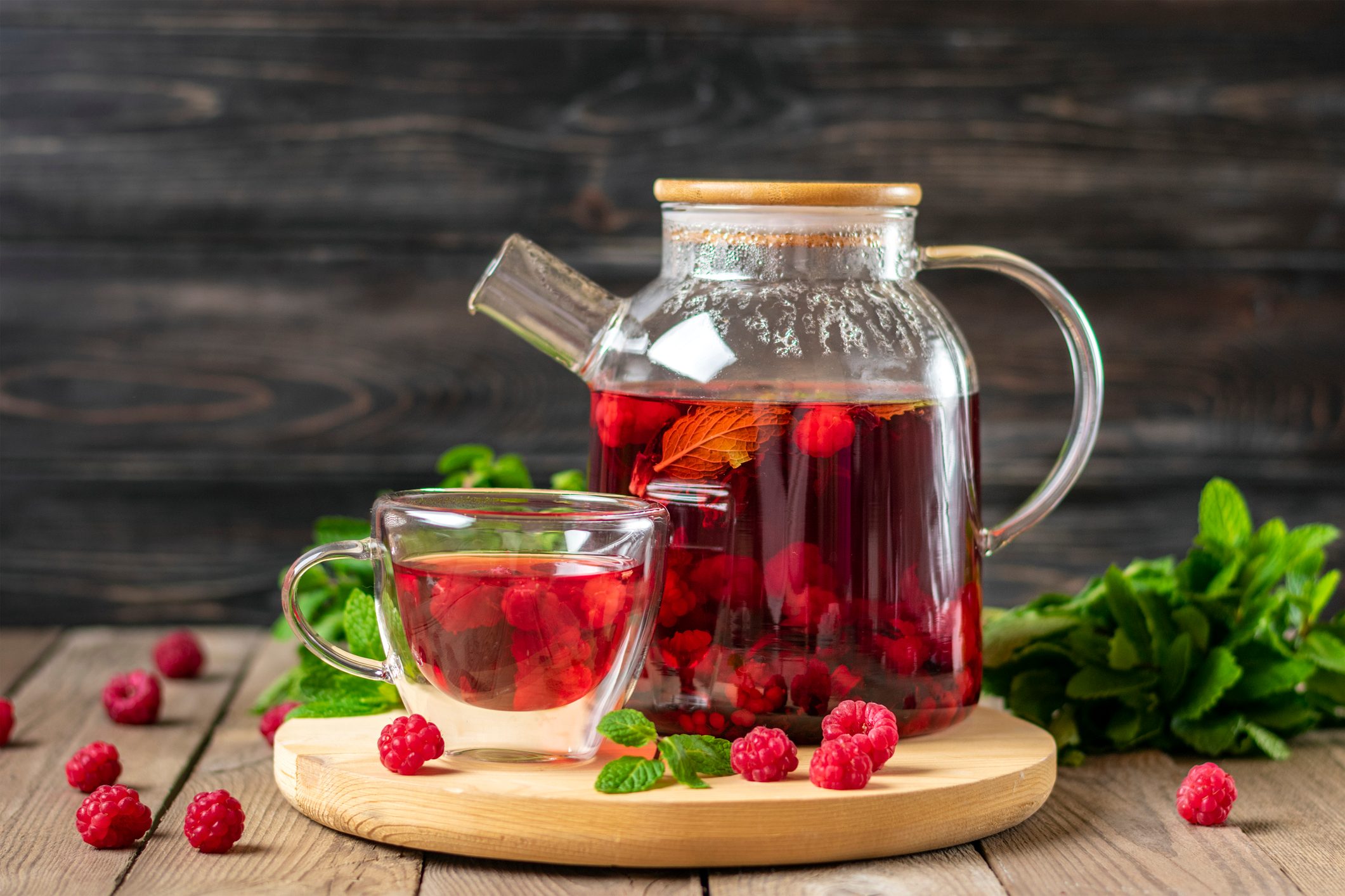 Herbal tea with berries, raspberries, mint leaves and hibiscus flowers in glass teapot and cup on wooden table Medicine for cold Vitamin drink Rustic style