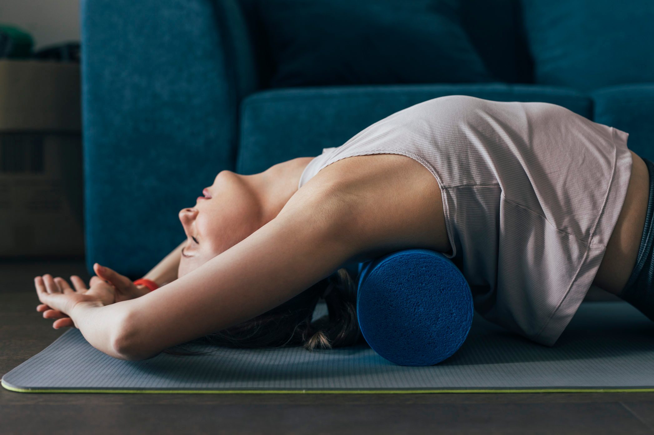 Working Out at Home Woman is Sportswear Using a Roller to Massage Back Muscles