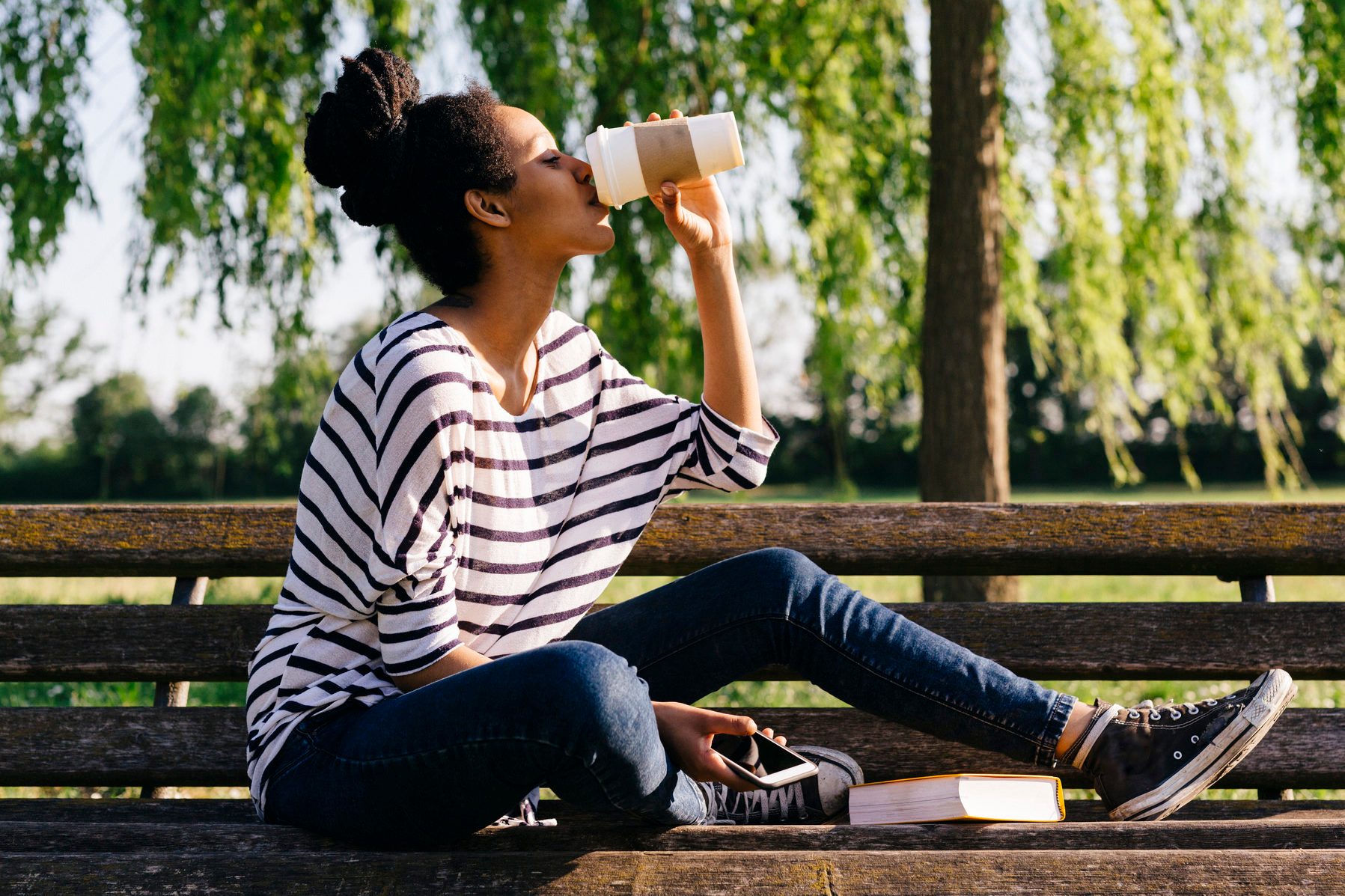 Young woman sitting on park bench drinking coffee to go