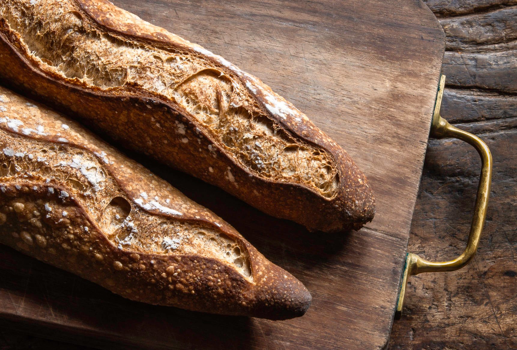 Two baguettes over a wood board on an old piece of wood