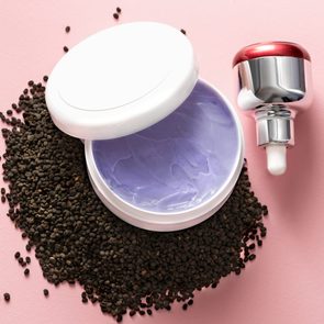 Babchi dry raw seeds (Psoralea Corylifolia) on pink surface with various kinds of cosmetic products. Bakuchiol cosmetics concept.